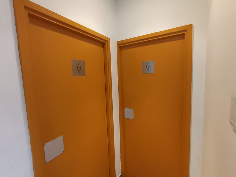 A hallway featuring two distinct orange doors with gender-specific signage, indicating access to separate restroom facilities within the industrial property.