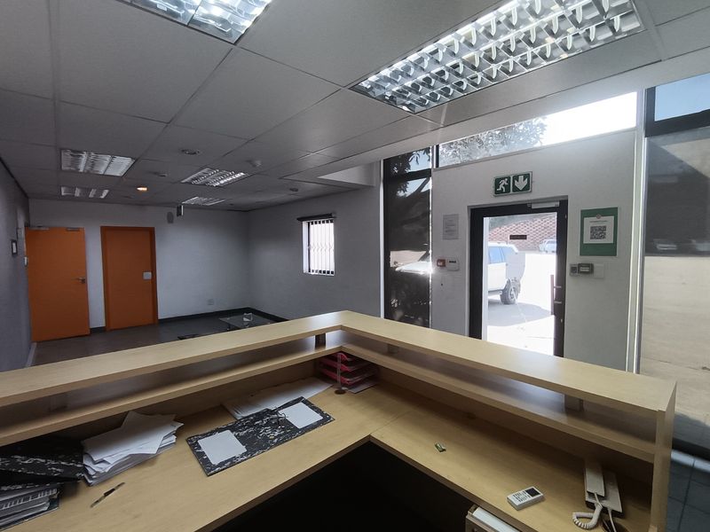 A bright, functional industrial reception area featuring a built-in desk, suspended ceiling with recessed lighting, and direct access to the exterior.