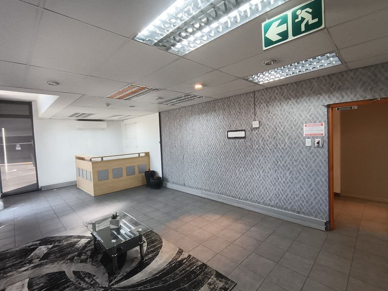 Industrial office reception area featuring a built-in reception desk, tiled flooring, suspended ceiling with integrated lighting, and an emergency exit sign.