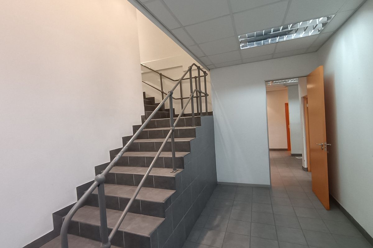A clean, functional industrial hallway featuring a tiled staircase with metal handrails, suspended ceiling, and neutral finishes.