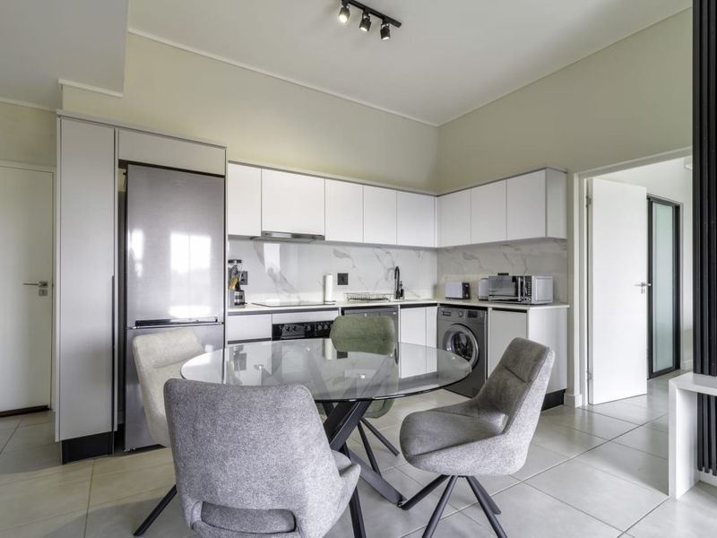 Modern open-plan kitchen featuring sleek white cabinetry, marble-look splashback, integrated appliances, and tiled flooring, seamlessly flowing into the dining area.