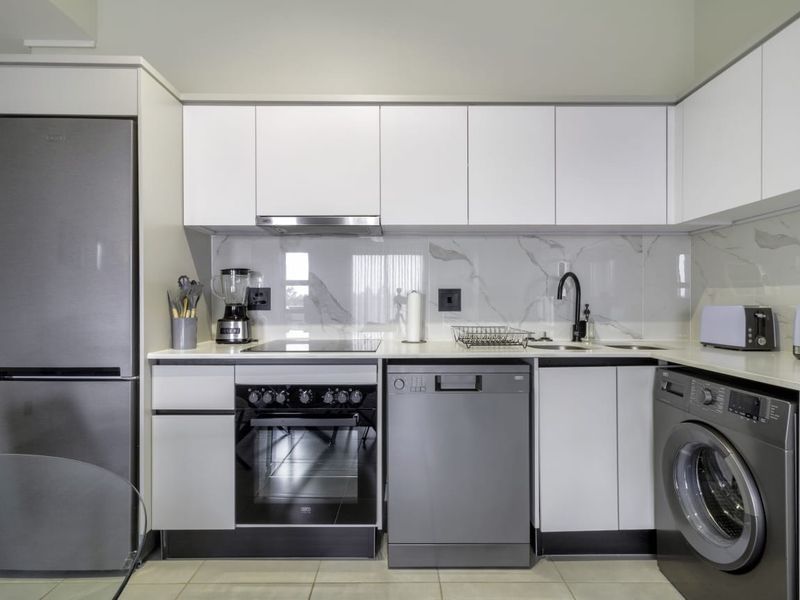 Modern kitchen featuring sleek white cabinetry, marble-look splashback, stone countertops, and high-quality integrated appliances including an oven, hob, and extractor fan.