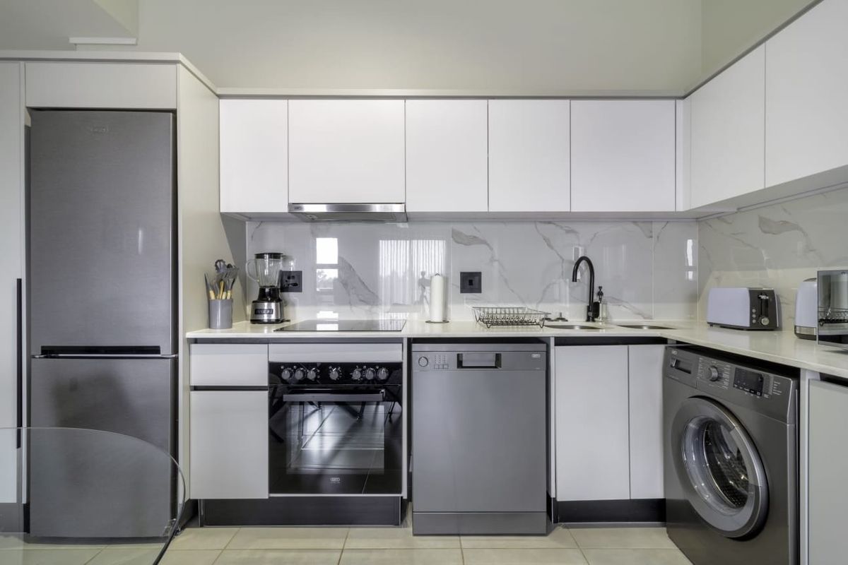 Modern kitchen featuring sleek white cabinetry, marble-look splashback, stone countertops, and high-quality integrated appliances including an oven, hob, and extractor fan.