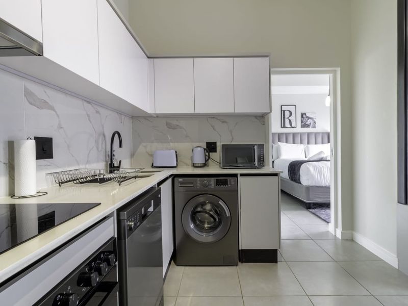 Modern kitchen featuring sleek white cabinetry, marble-look splashback, stone countertops, and integrated appliances, including a washing machine and dishwasher.