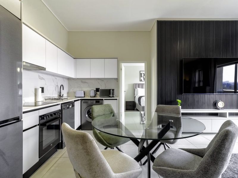 Modern open-plan kitchen and living area featuring sleek white cabinetry, marble-look splashback, integrated appliances, and a contemporary slatted feature wall.