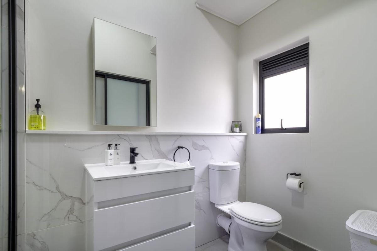 Modern bathroom featuring a sleek vanity cabinet, marble-look wall tiling, wall-mounted mirror, and a contemporary toilet.