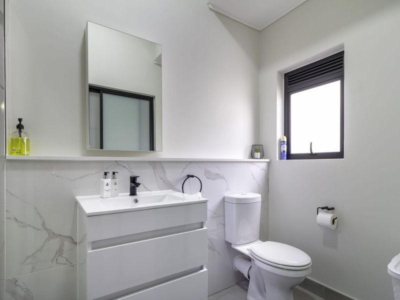 Modern bathroom featuring a sleek vanity cabinet, marble-look wall tiling, wall-mounted mirror, and a contemporary toilet.
