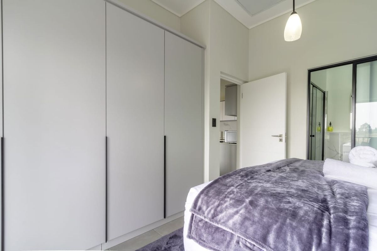 A modern bedroom featuring floor-to-ceiling built-in wardrobes, neutral finishes, and direct access to an en-suite bathroom.