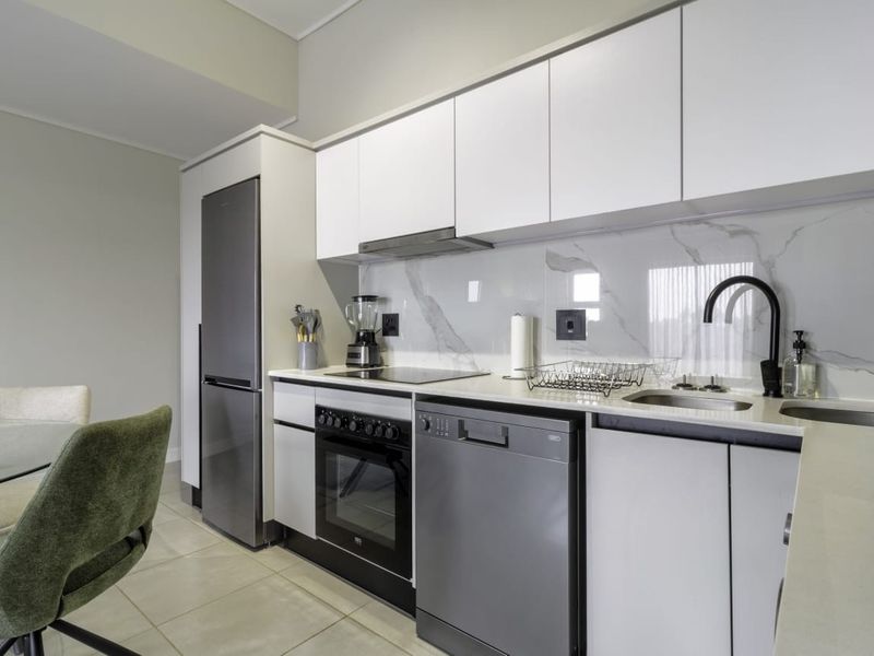 Modern kitchen featuring sleek white cabinetry, stone countertops, marble-look splashback, and high-quality integrated appliances including an oven, hob, and extractor fan.