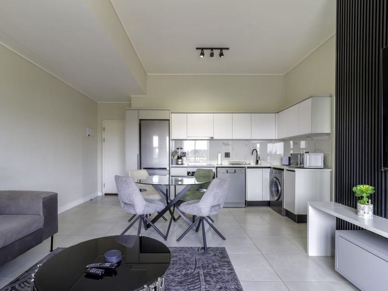 Modern open-plan living area featuring a sleek kitchen with white cabinetry, integrated appliances, tiled flooring, and a contemporary slatted feature wall.