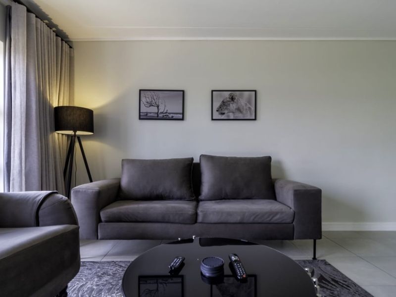 A well-maintained living room featuring neutral wall tones, tiled flooring, and floor-to-ceiling curtains.