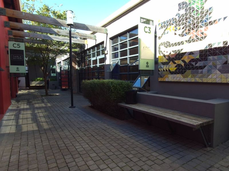 A well-maintained outdoor courtyard area featuring a timber pergola, paved walkway, built-in bench seating, and decorative mosaic wall art.