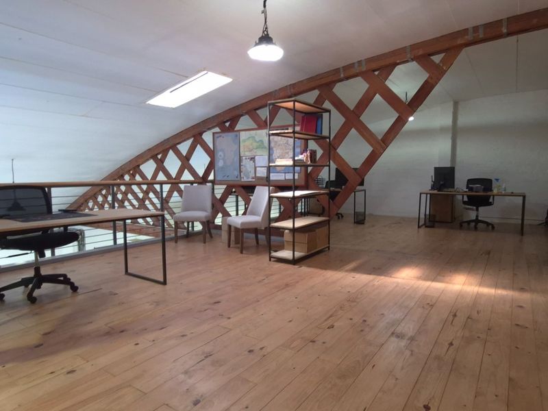 Spacious open-plan office area featuring exposed timber roof trusses, warm timber flooring, a skylight, and an exposed brick feature wall.