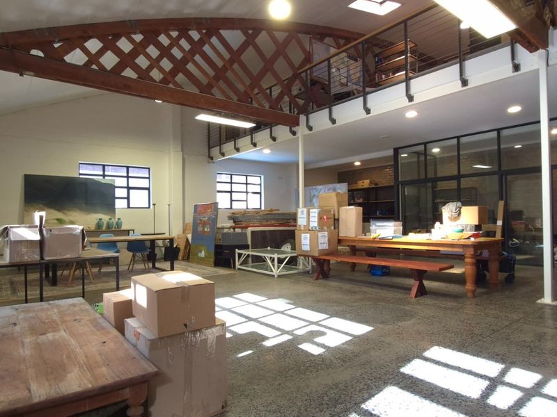 Spacious open-plan retail or studio area featuring high ceilings with exposed timber trusses, a mezzanine level, and polished concrete floors.