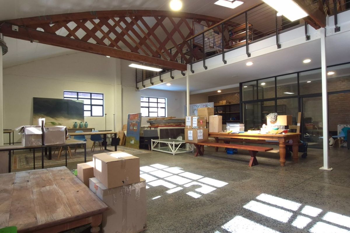 Spacious open-plan retail or studio area featuring high ceilings with exposed timber trusses, a mezzanine level, and polished concrete floors.