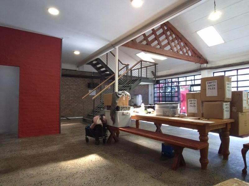 Spacious open-plan retail or office area featuring industrial design elements, including exposed brickwork, timber roof trusses, polished concrete floors, and a feature steel staircase.