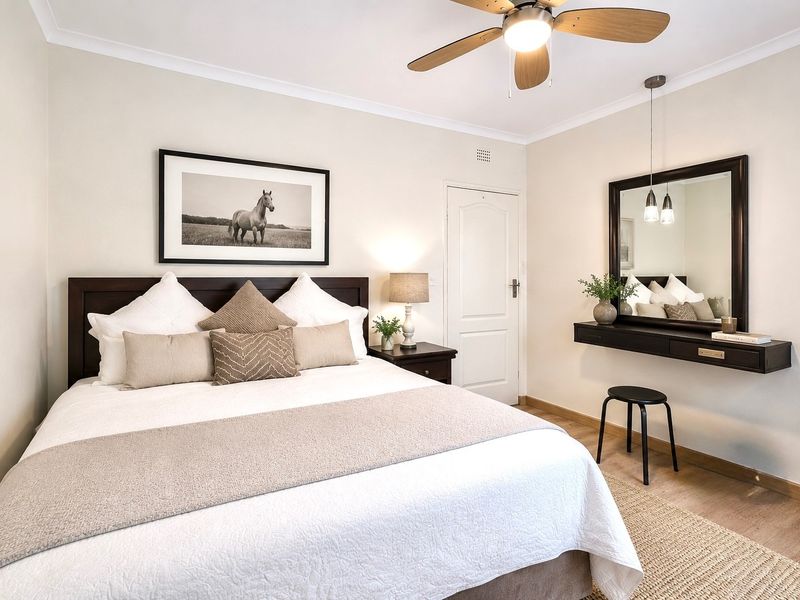 A well-maintained bedroom featuring a ceiling fan, neutral wall finishes, and a built-in floating vanity with integrated mirror.