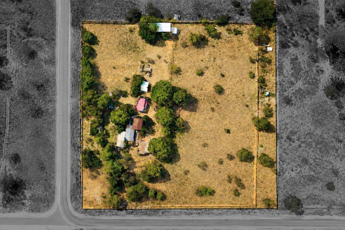 Aerial view of a large rural plot featuring perimeter fencing, mature trees, and several small outbuildings requiring maintenance.