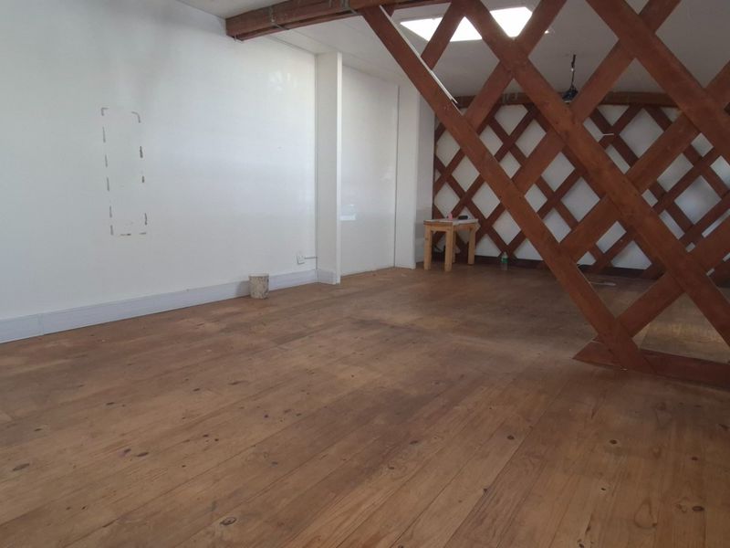 An empty office space featuring timber flooring, a decorative timber lattice partition, and a skylight providing natural illumination.
