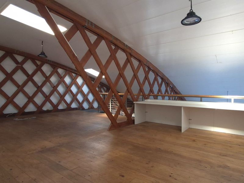 Spacious open-plan office area featuring unique timber lattice roof architecture, hardwood flooring, built-in desk space, and natural light from multiple skylights.