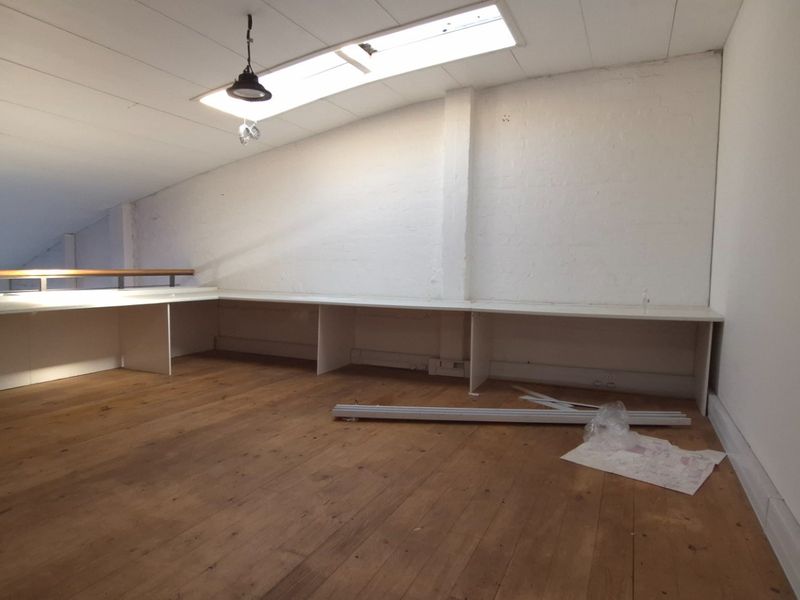 An empty office space featuring timber flooring, a built-in desk, and a skylight, providing a functional workspace with natural light.