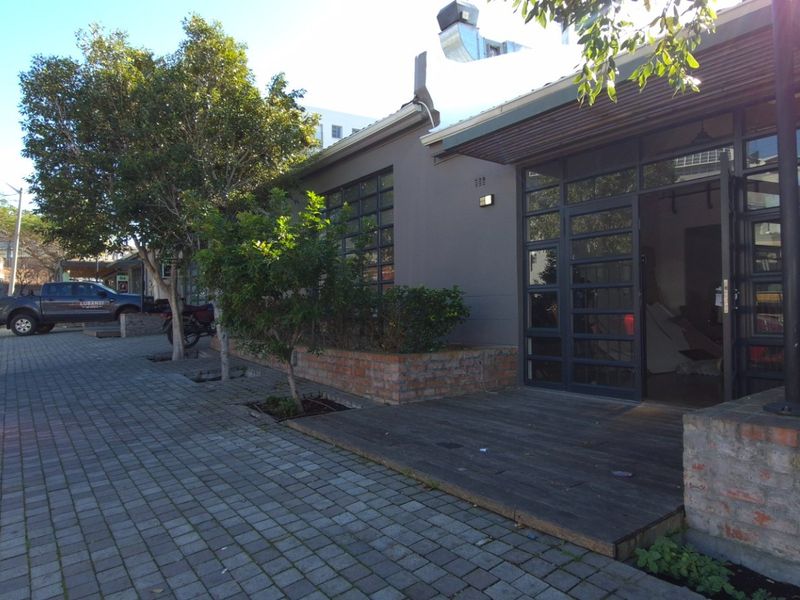 Front facade of a commercial property featuring industrial-style steel-framed glass doors, timber decking, and brick planter boxes along the paved street frontage.