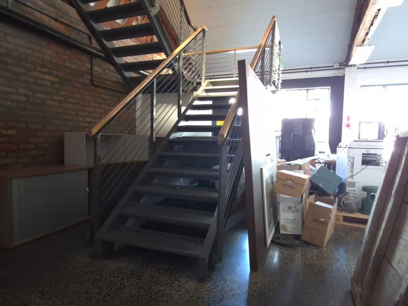 Industrial-style commercial hallway featuring an exposed brick wall, polished concrete flooring, and a modern metal staircase with steel cable railings.