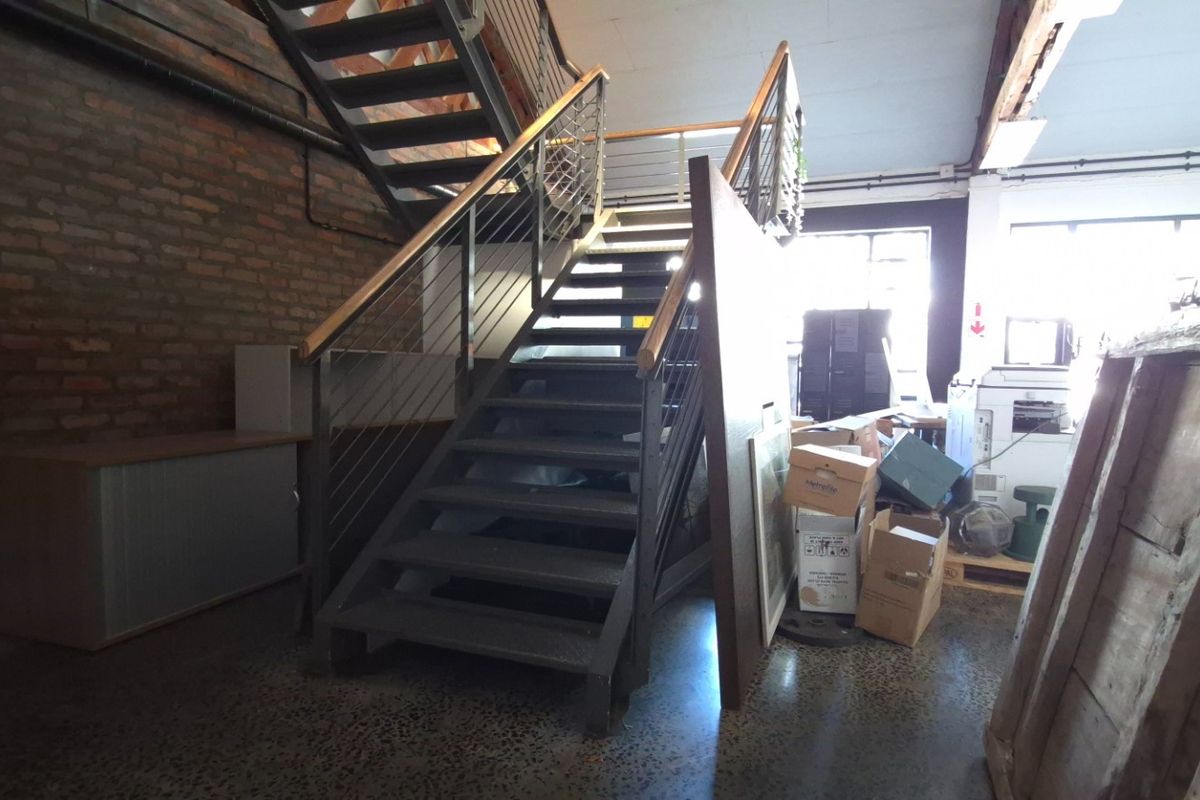 Industrial-style commercial hallway featuring an exposed brick wall, polished concrete flooring, and a modern metal staircase with steel cable railings.