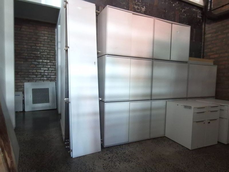 A utility or storage area featuring exposed brick walls, polished concrete floors, and built-in white cabinetry.