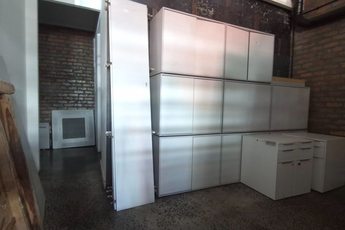 A utility or storage area featuring exposed brick walls, polished concrete floors, and built-in white cabinetry.