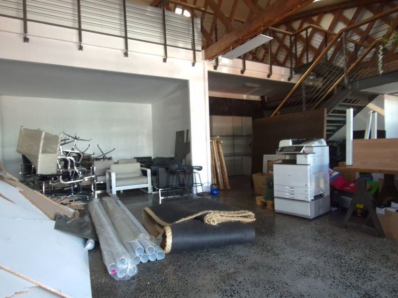 Spacious open-plan commercial area featuring a mezzanine level, exposed timber roof trusses, steel staircase, and polished concrete flooring.
