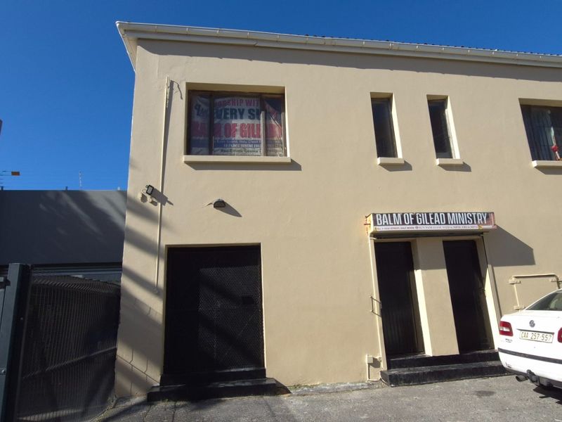 Front facade of a two-story commercial building featuring security gates, security bars on windows, and a paved driveway area.