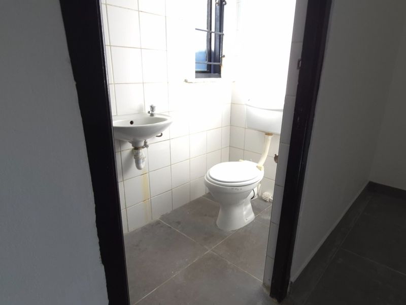 A compact, empty bathroom featuring a wall-mounted basin, toilet, and tiled finishes, requiring minor maintenance and cosmetic updates.