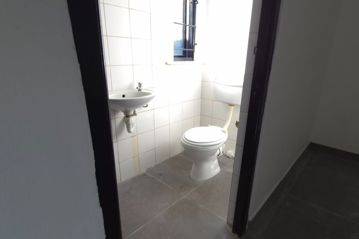 A compact, empty bathroom featuring a wall-mounted basin, toilet, and tiled finishes, requiring minor maintenance and cosmetic updates.