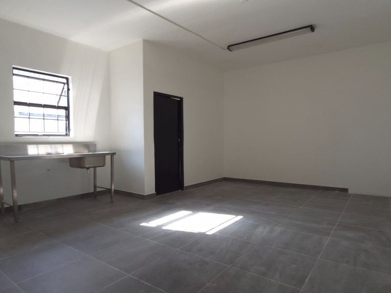 A clean, empty utility space featuring tiled flooring, a stainless steel sink, and a security window, suitable for various commercial or storage purposes.