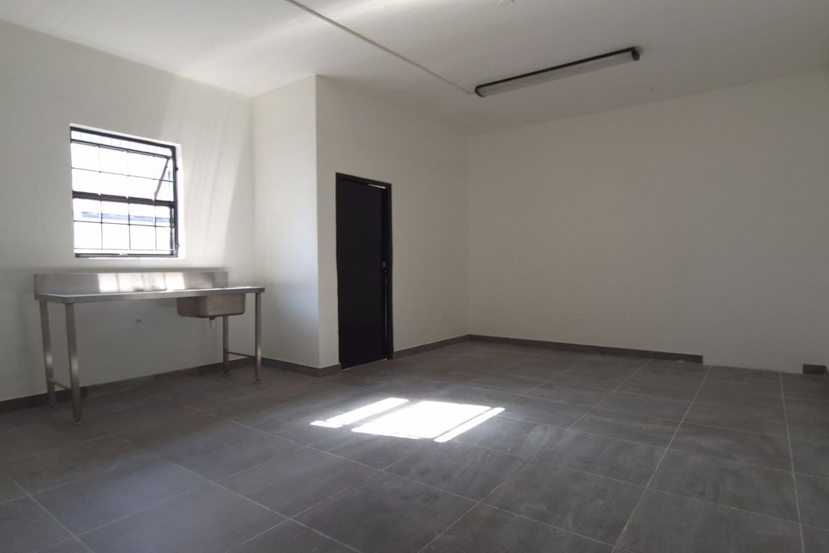 A clean, empty utility space featuring tiled flooring, a stainless steel sink, and a security window, suitable for various commercial or storage purposes.