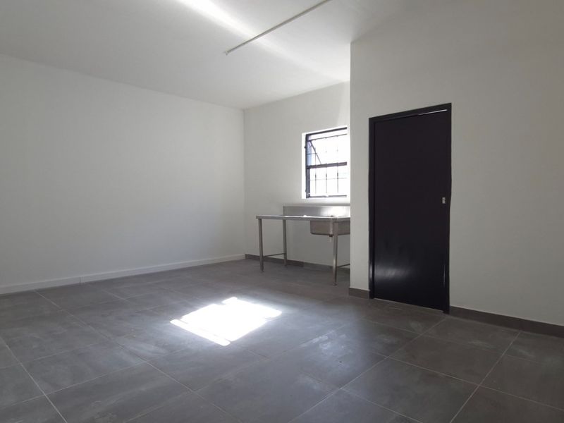 A clean, vacant utility space featuring grey tiled flooring, a stainless steel sink, and neutral white walls, suitable for various commercial or storage purposes.