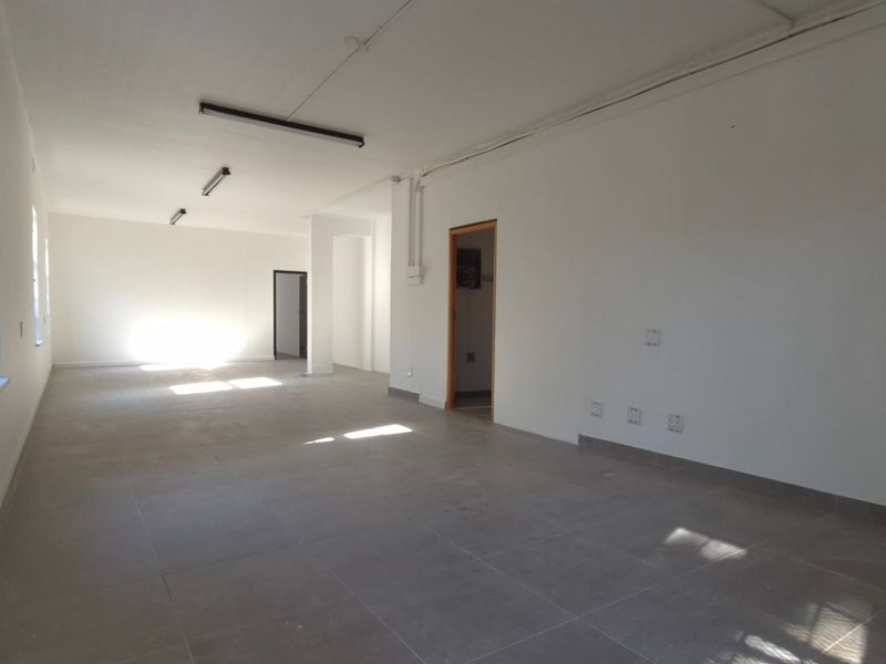 A spacious, empty open-plan retail unit featuring neutral tiled flooring, white walls, and functional overhead lighting, ready for custom fit-out.