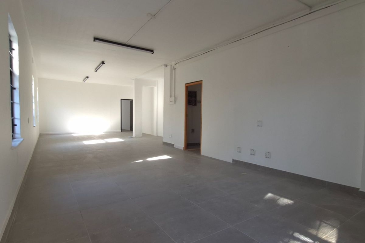 A spacious, empty open-plan retail unit featuring neutral tiled flooring, white walls, and functional overhead lighting, ready for custom fit-out.