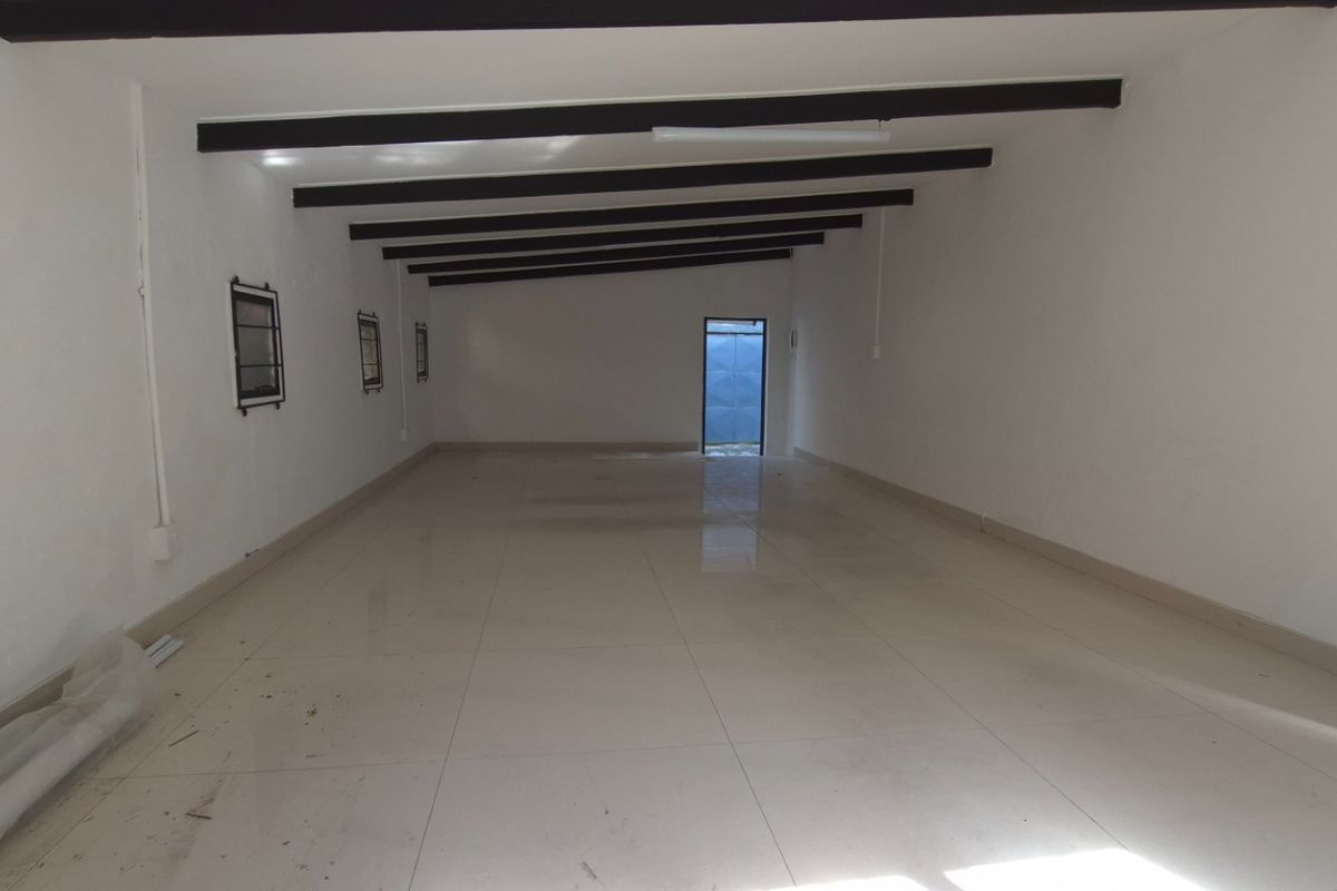 A spacious, empty open-plan retail area featuring tiled flooring, exposed ceiling beams, and multiple windows with security bars.