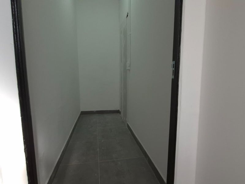 A clean, empty hallway featuring neutral wall finishes and modern grey floor tiles, providing a simple transition space within the retail property.