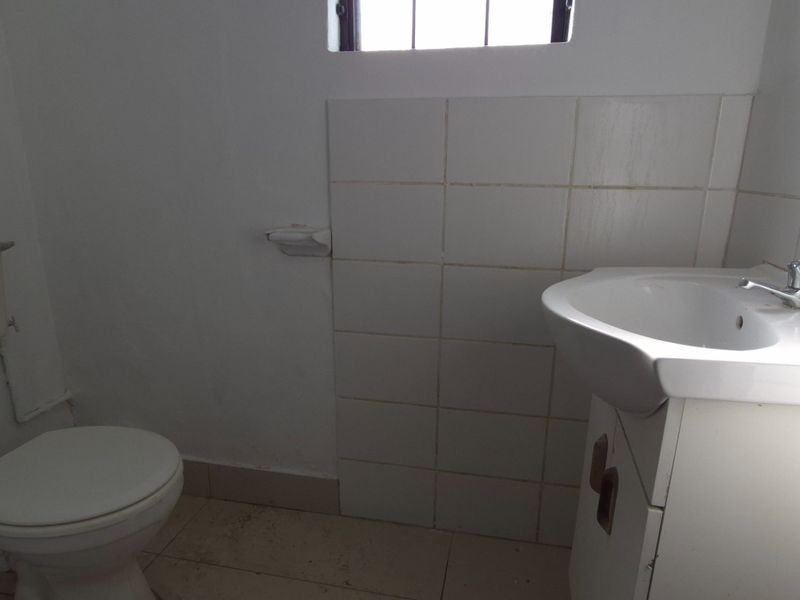 A compact bathroom featuring a white ceramic washbasin with vanity cabinet, toilet, and tiled splashback, requiring minor cosmetic updates.