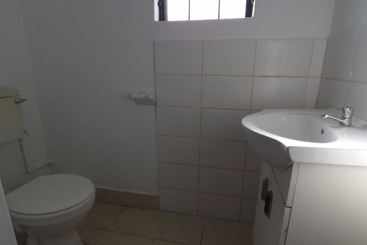A compact bathroom featuring a white ceramic washbasin with vanity cabinet, toilet, and tiled splashback, requiring minor cosmetic updates.