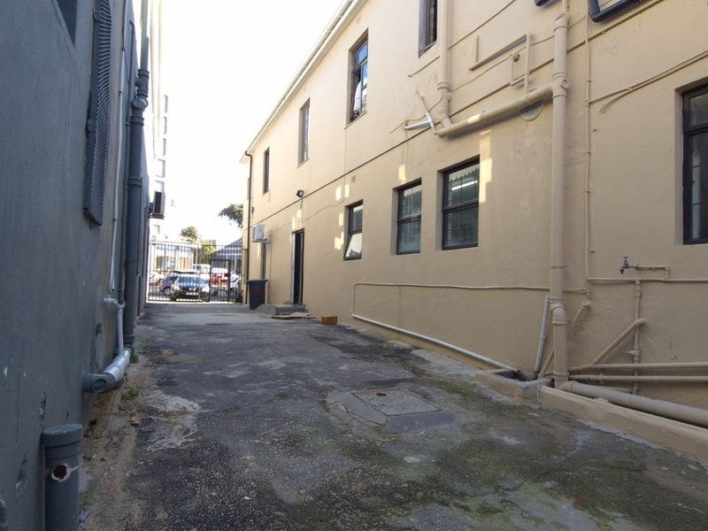 Rear exterior alleyway showing building facade, external plumbing, and paved access area with security gate.