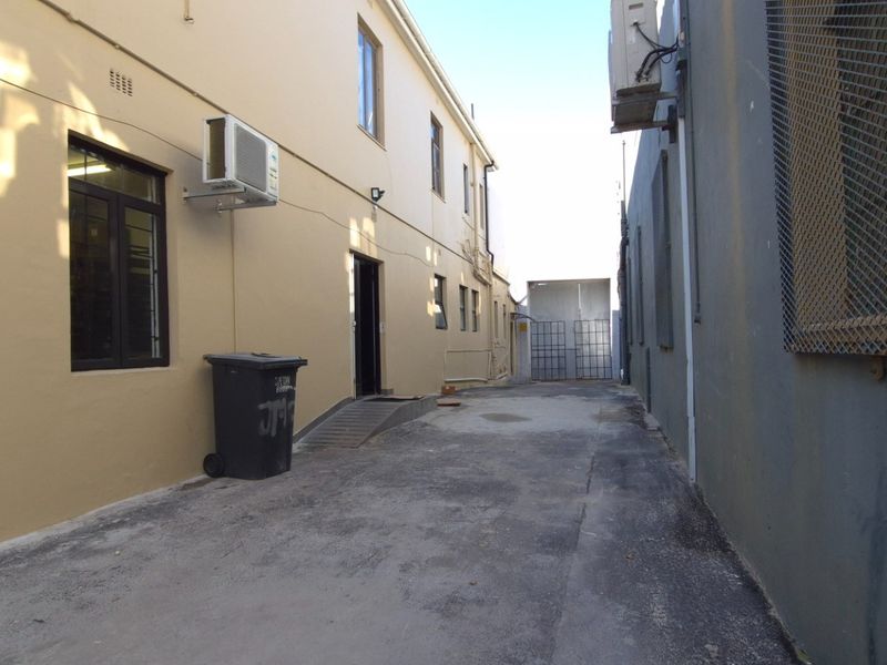 Rear exterior service alleyway featuring paved access, security gates, and wall-mounted air conditioning units for the retail property.