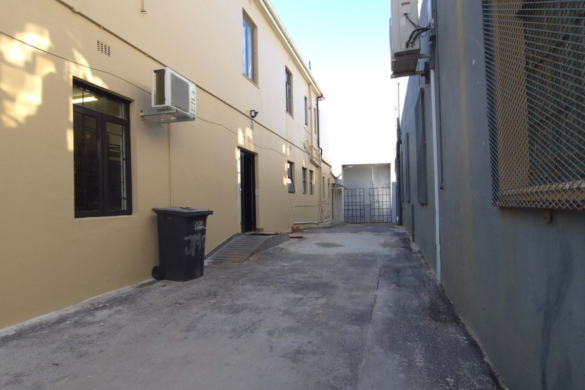 Rear exterior service alleyway featuring paved access, security gates, and wall-mounted air conditioning units for the retail property.