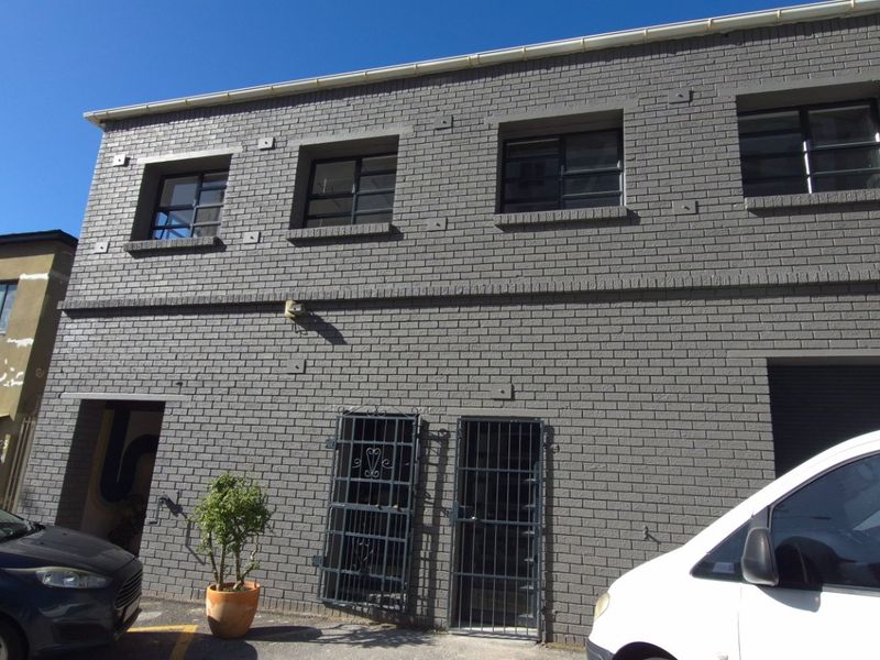 Front elevation of a two-story commercial building featuring a grey brick facade, secure metal entry gates, and window security bars.