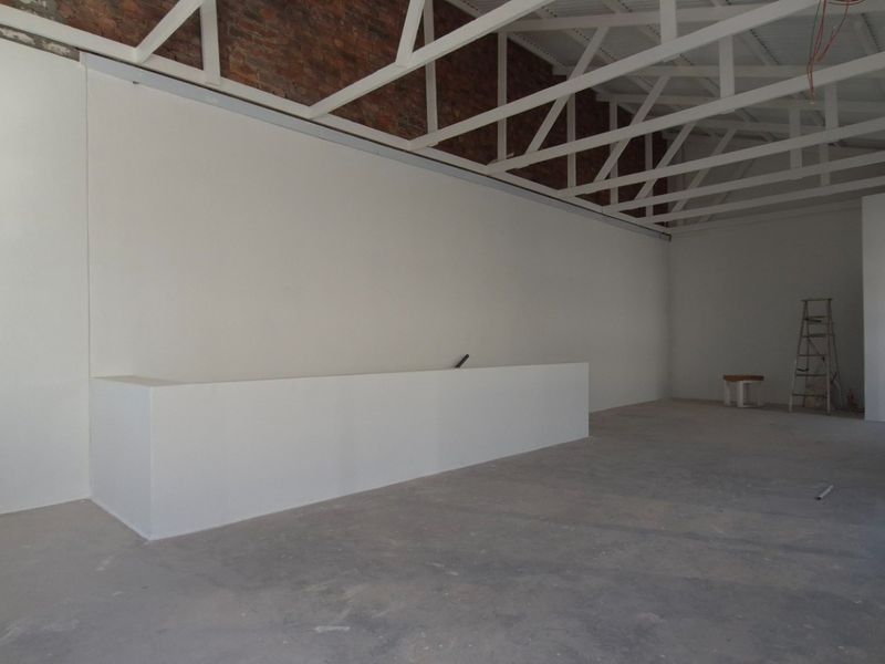 Spacious open-plan retail area featuring exposed brickwork, high vaulted ceilings with white trusses, and a built-in service counter in a shell condition.