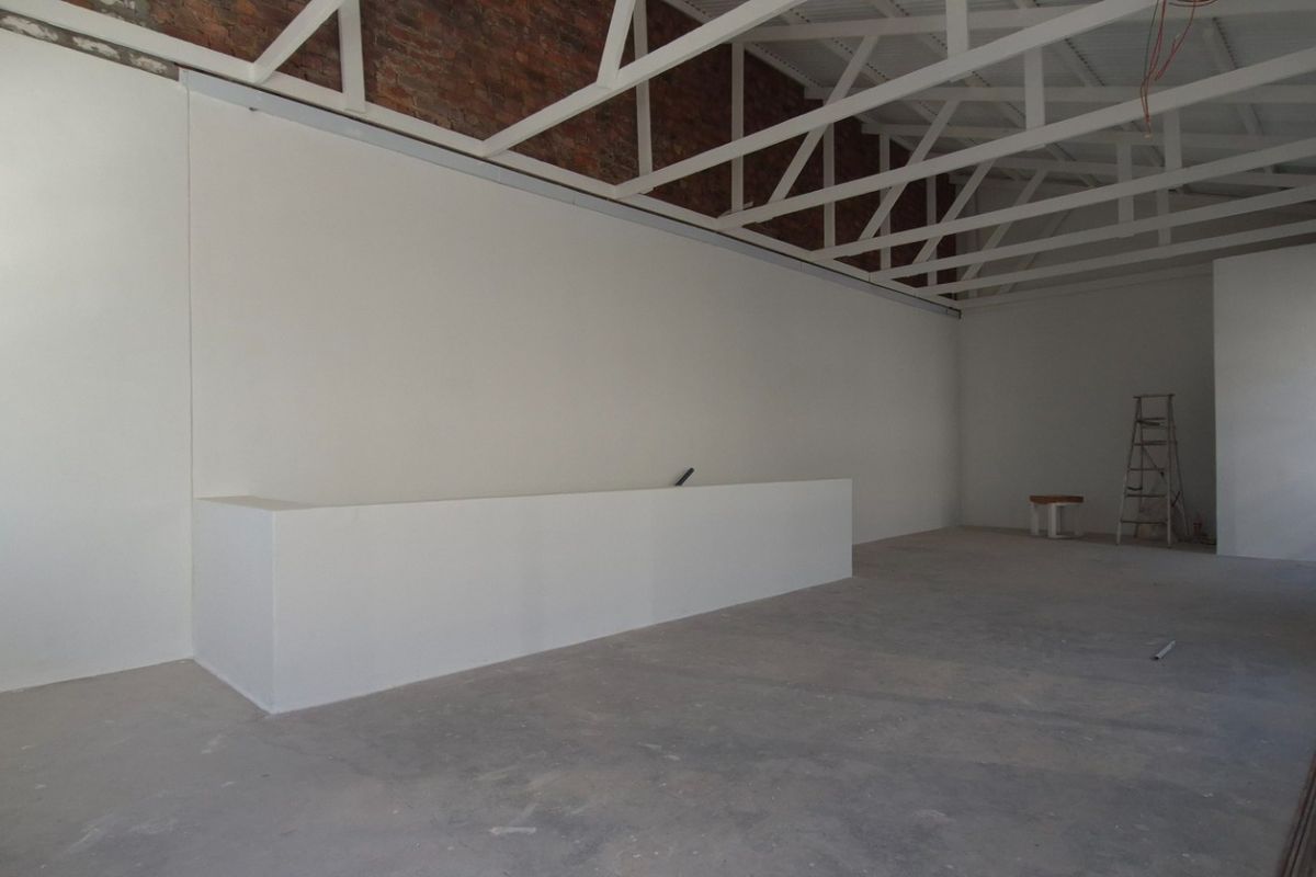 Spacious open-plan retail area featuring exposed brickwork, high vaulted ceilings with white trusses, and a built-in service counter in a shell condition.