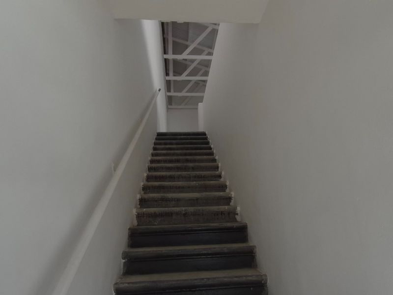 A narrow interior staircase leading to an upper level with exposed roof trusses and plain white walls.